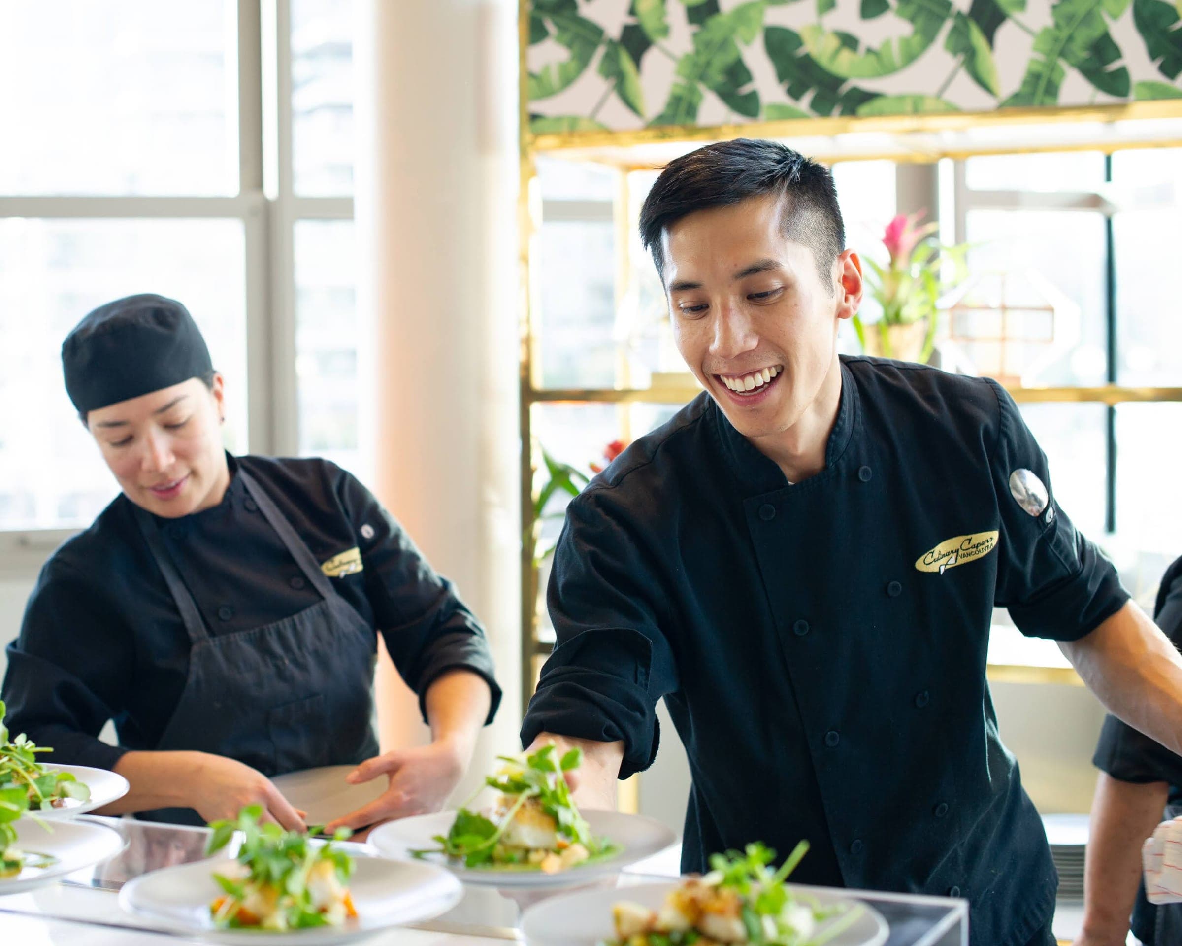 Two chefs smiling as they plate a course together at an event